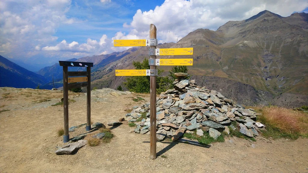 Palo con più cartelli gialli di segnaletica escursionistica su un sentiero di montagna