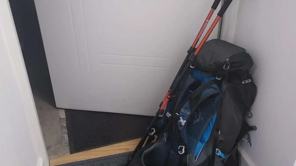Zaino da escursionismo con bastoncini da trekking e un paio di scarpe appoggiate accanto